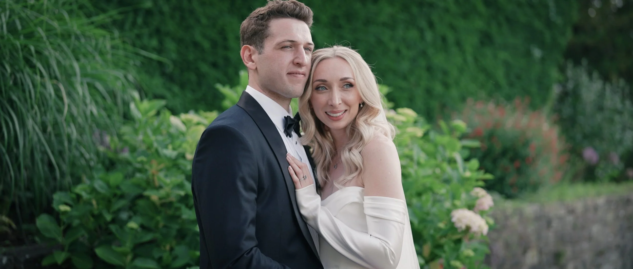 Hedsor House bride and groom standing in gardens in front of lush green florals.