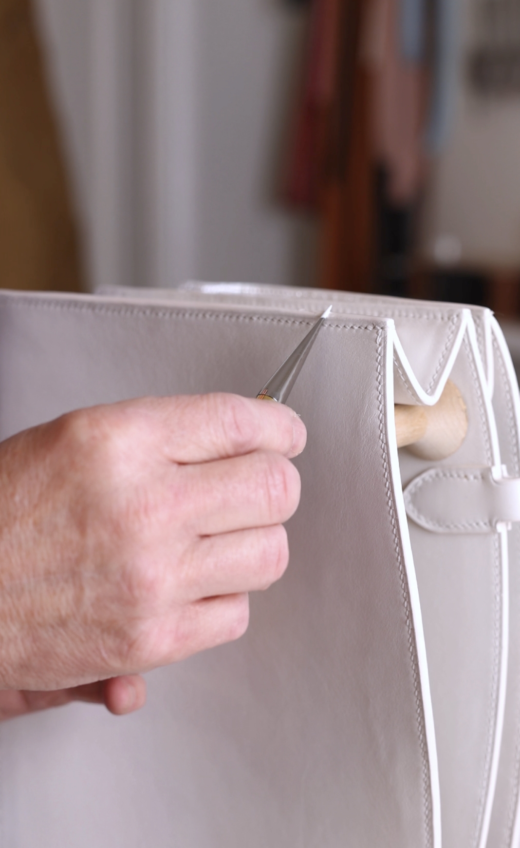 A person is applying edge finish on a white leather hand bag.