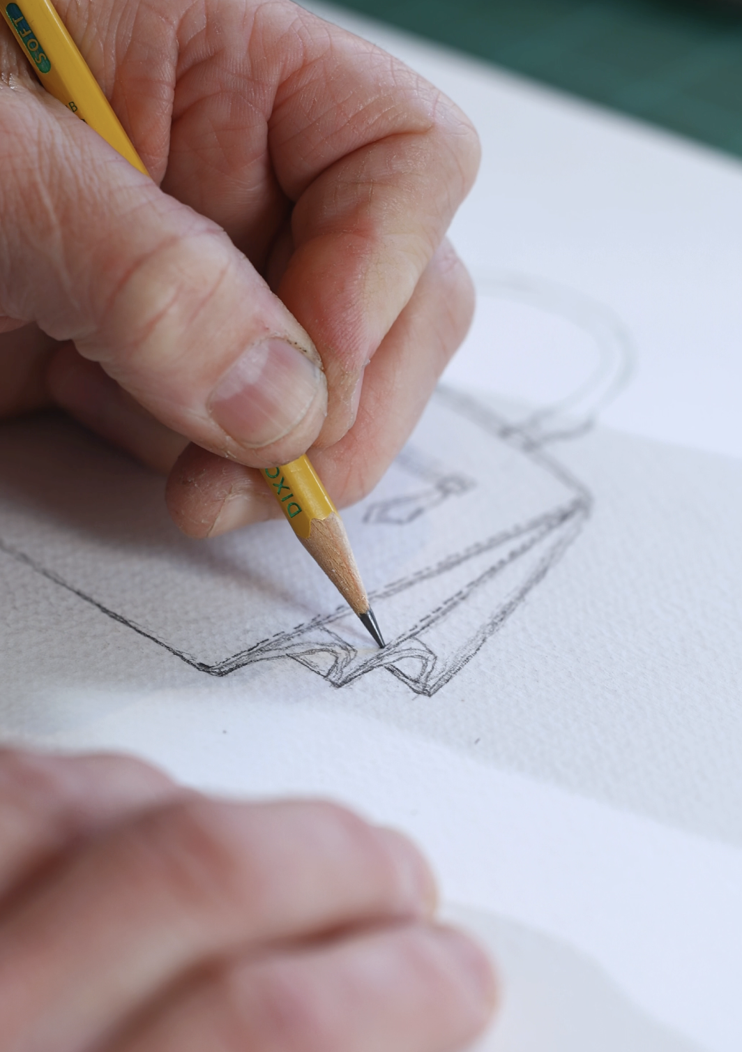 A person drawing or sketch of a hand bag on a white textured paper with a yellow and black pencil, showing close-up of their hand and the drawing.