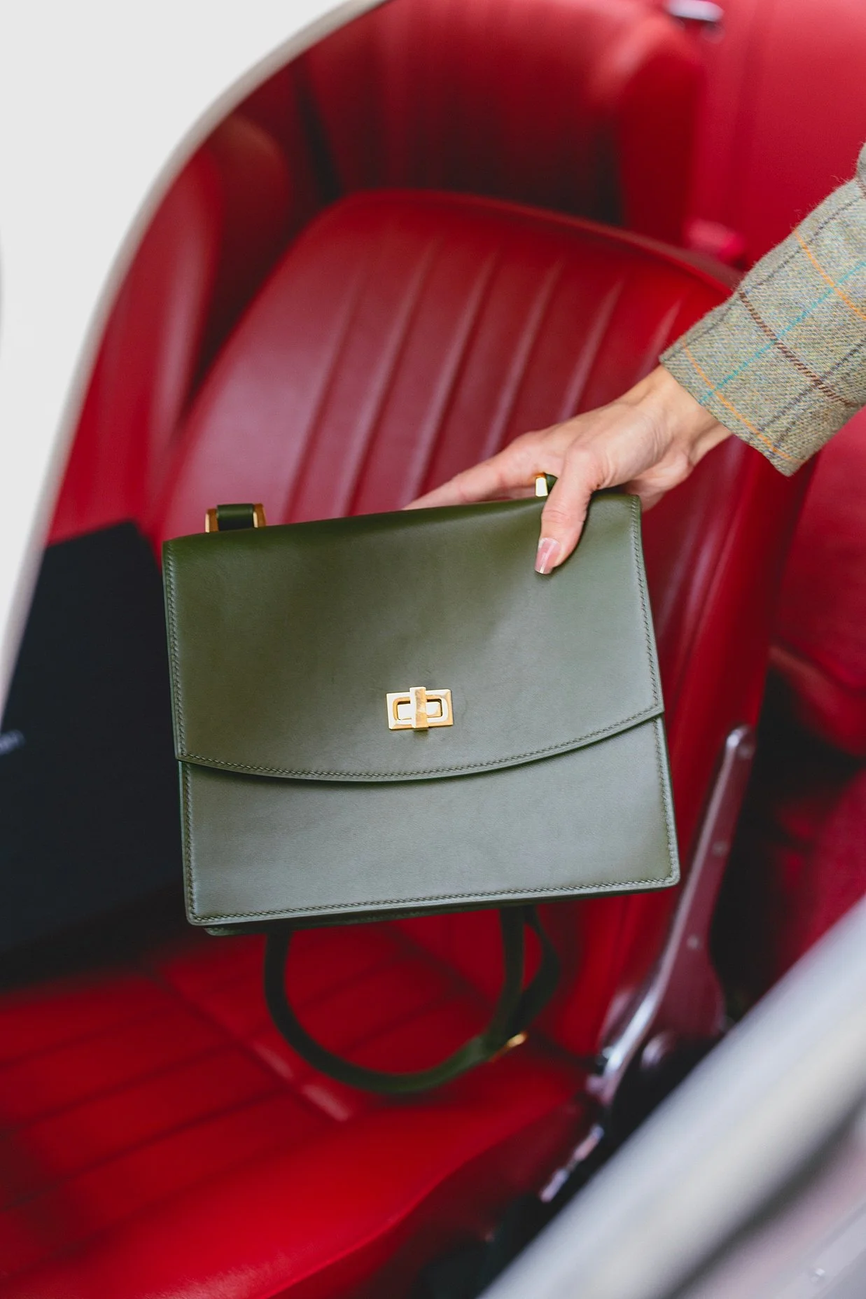 Person holding a green handbag with gold hardware, sitting on a red leather seat.