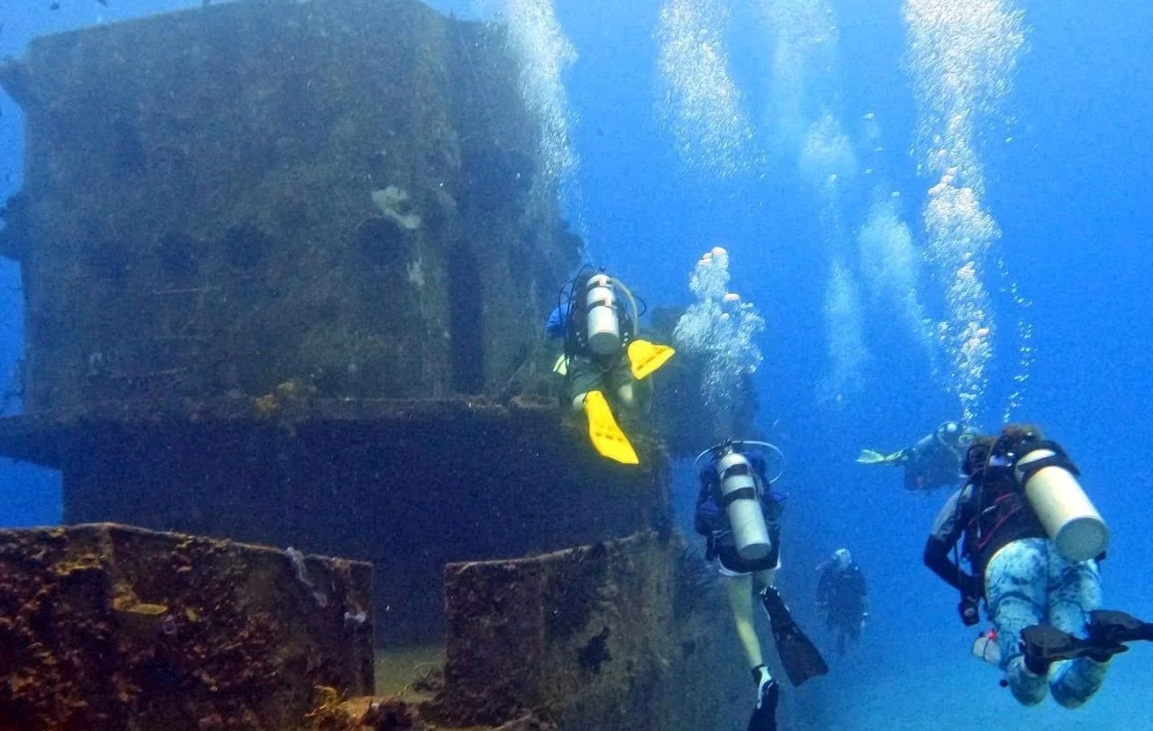 Group of scuba divers exploring underwater ruins with air bubbles rising to the surface