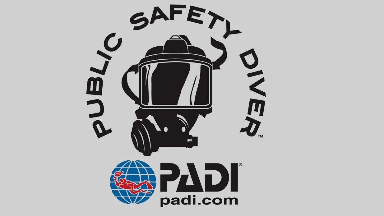 Logo for PADI Public Safety Diver, featuring a black and white dive helmet above the PADI logo, with the text 'Public Safety Diver' curved above the helmet and the website 'padi.com' below.