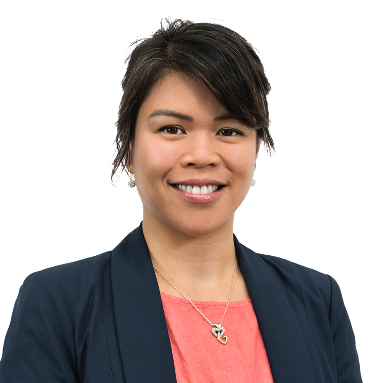 A smiling woman with short dark hair wearing a navy blazer over a coral top and a necklace with a fish-shaped pendant.