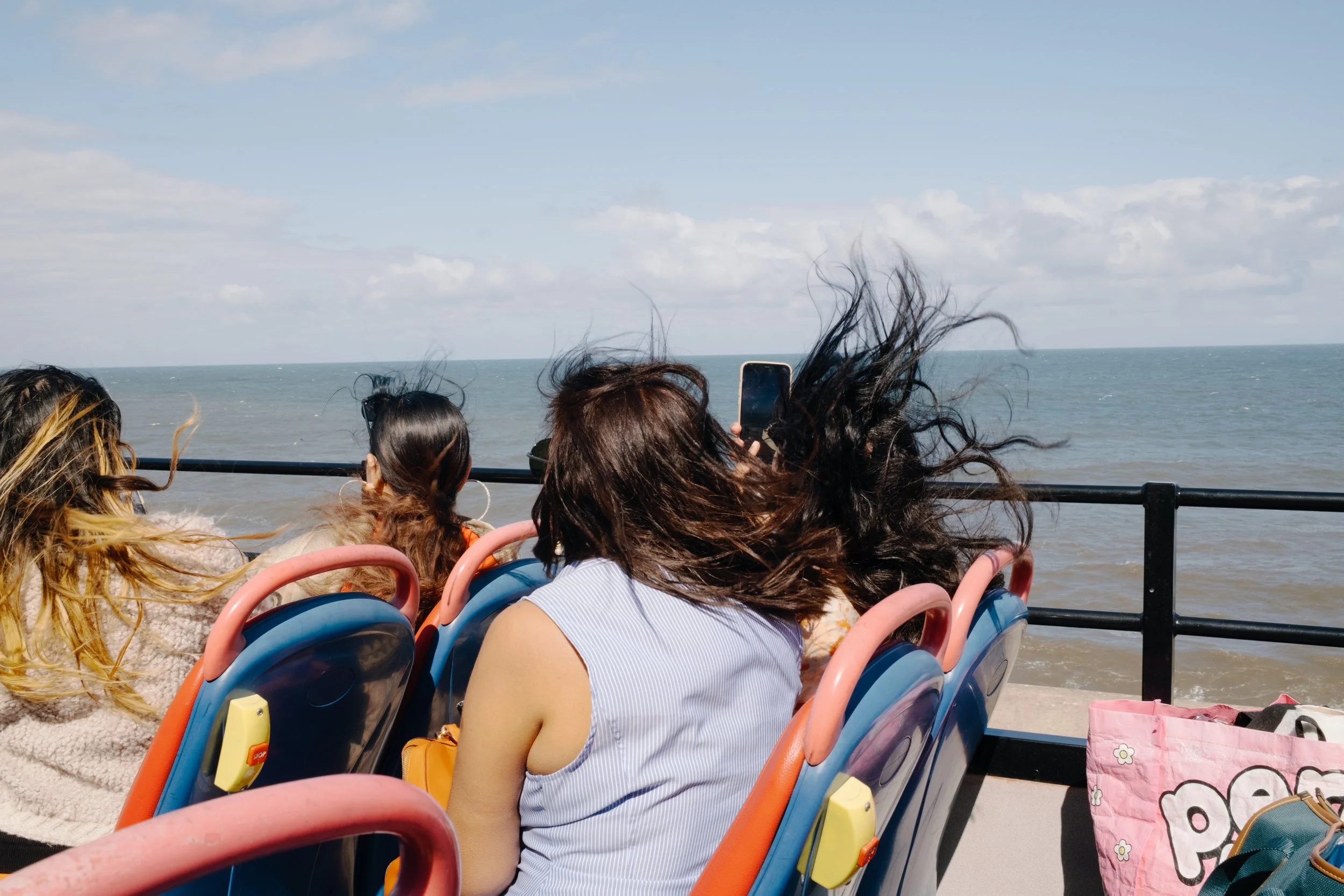 People on a boat or ferry enjoying a ride on the water, with their hair blowing in the wind and a view of the ocean and sky in the background.