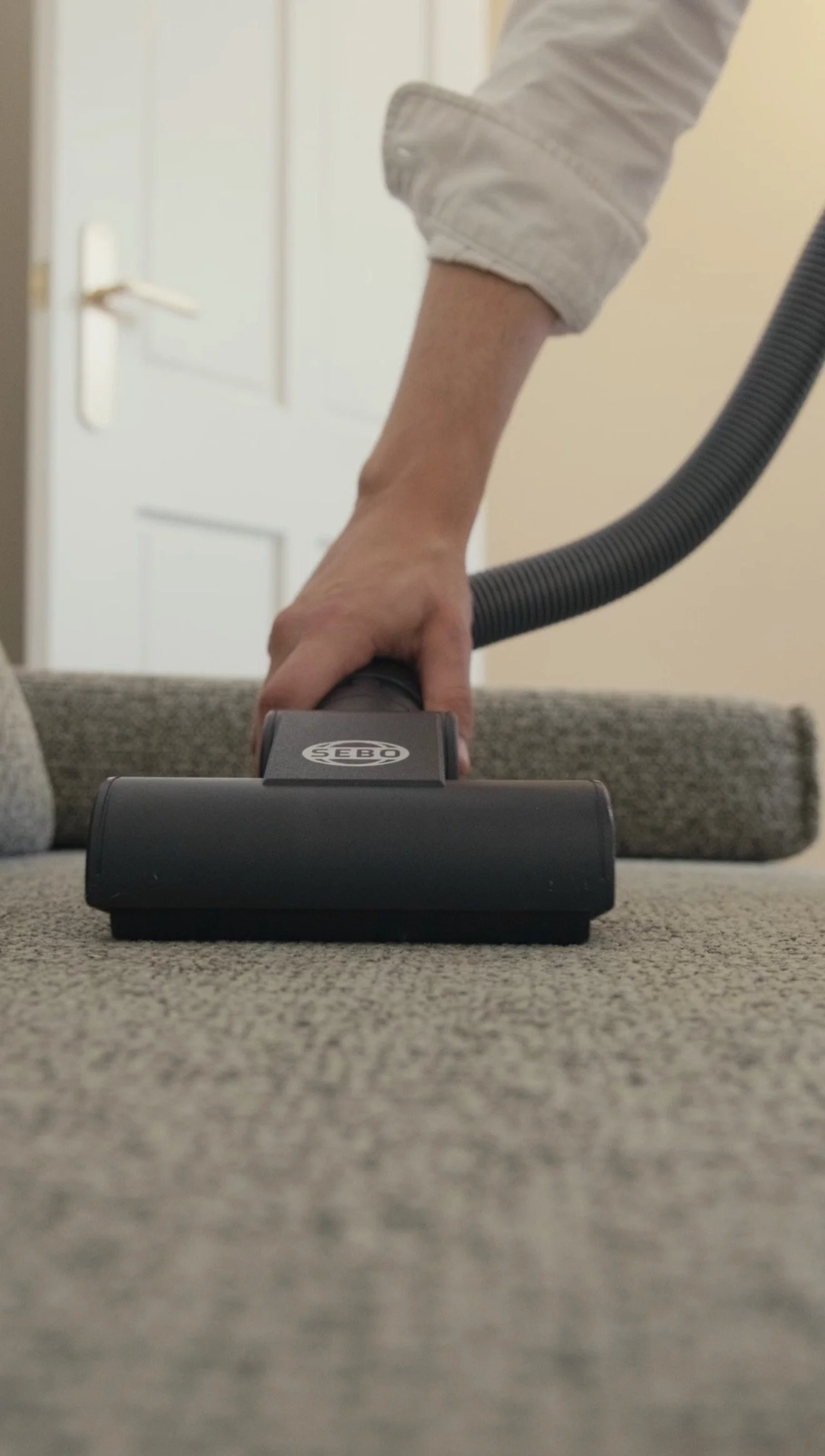 Close-up of a person's hand using a vacuum cleaner on a carpeted floor indoors.