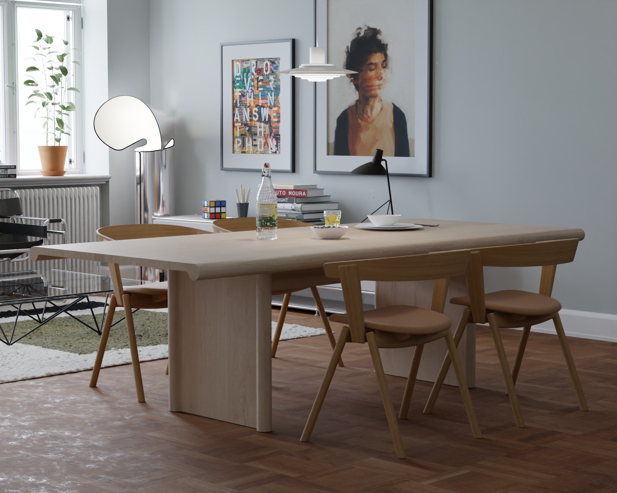 Modern dining room with a light wooden table and matching chairs, artwork on the walls, books, a Rubik's cube, and a water bottle on the table. Large window with a potted plant.