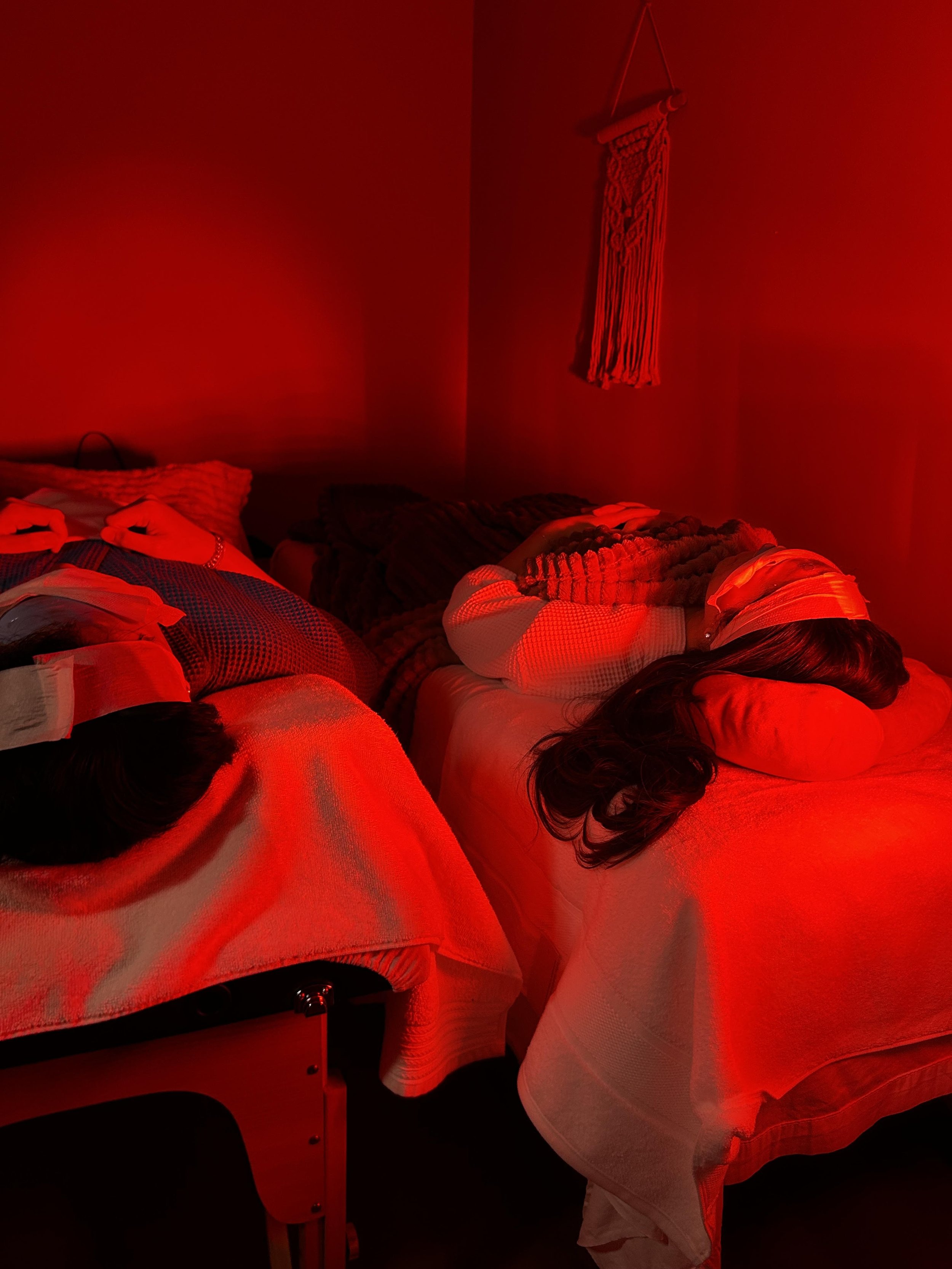 People lying on tables in a dark room illuminated by red light, with one person resting their head on a table.