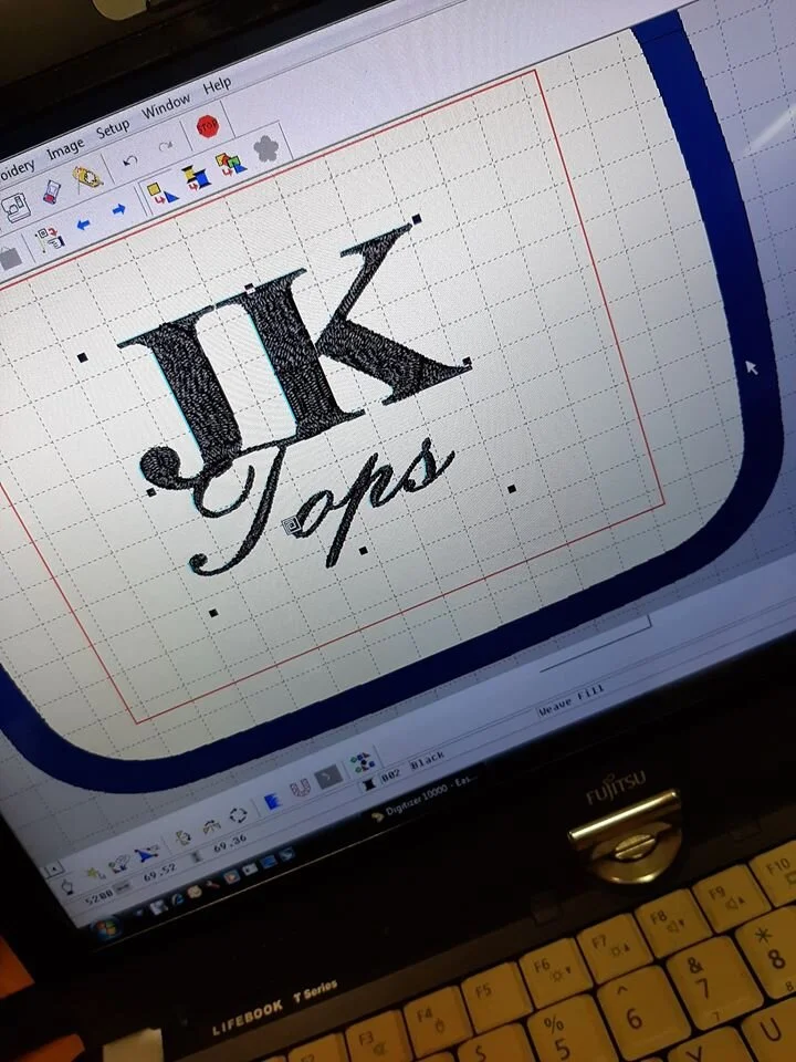 Digital embroidery design of the text 'JK Tops' on a computer screen, with the design in black against a grid background.
