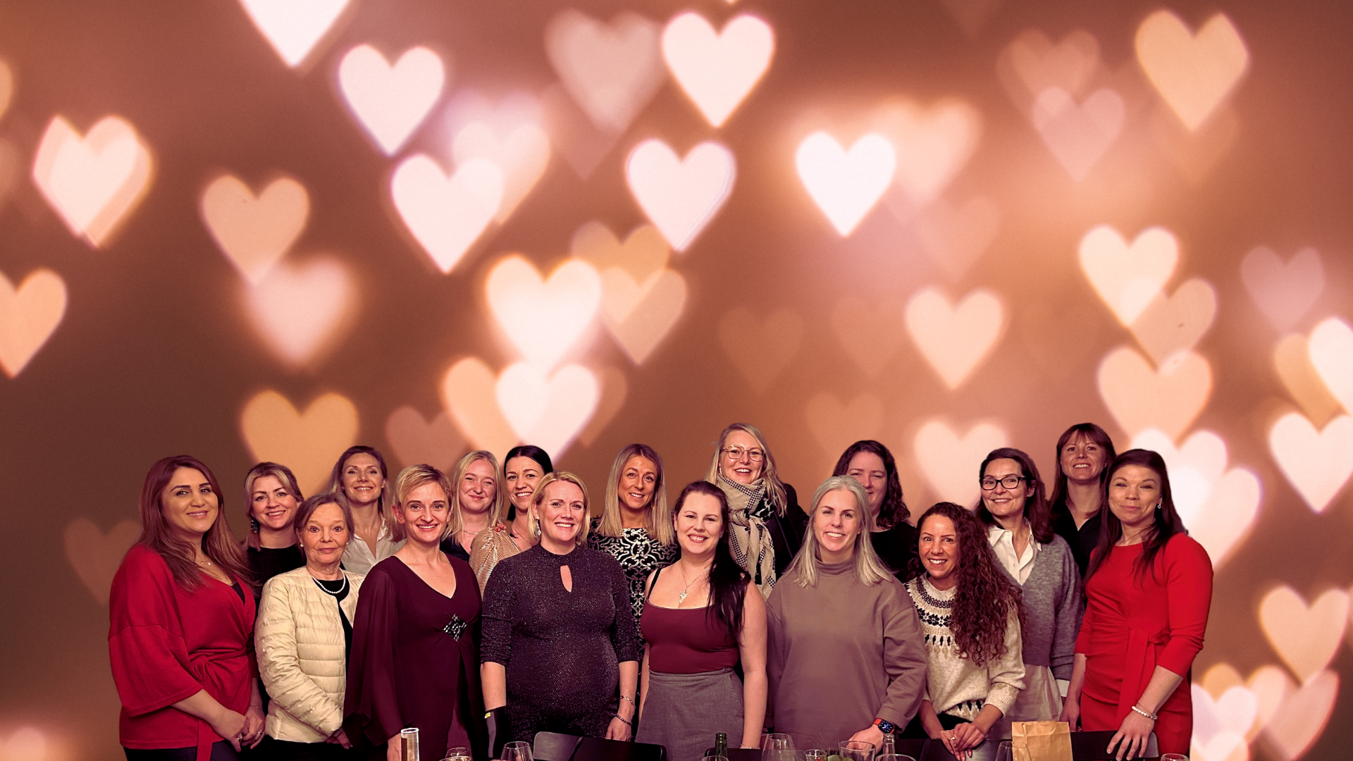 Grupp kvinnor ler framför en bakgrund med hjärtformade ljus.