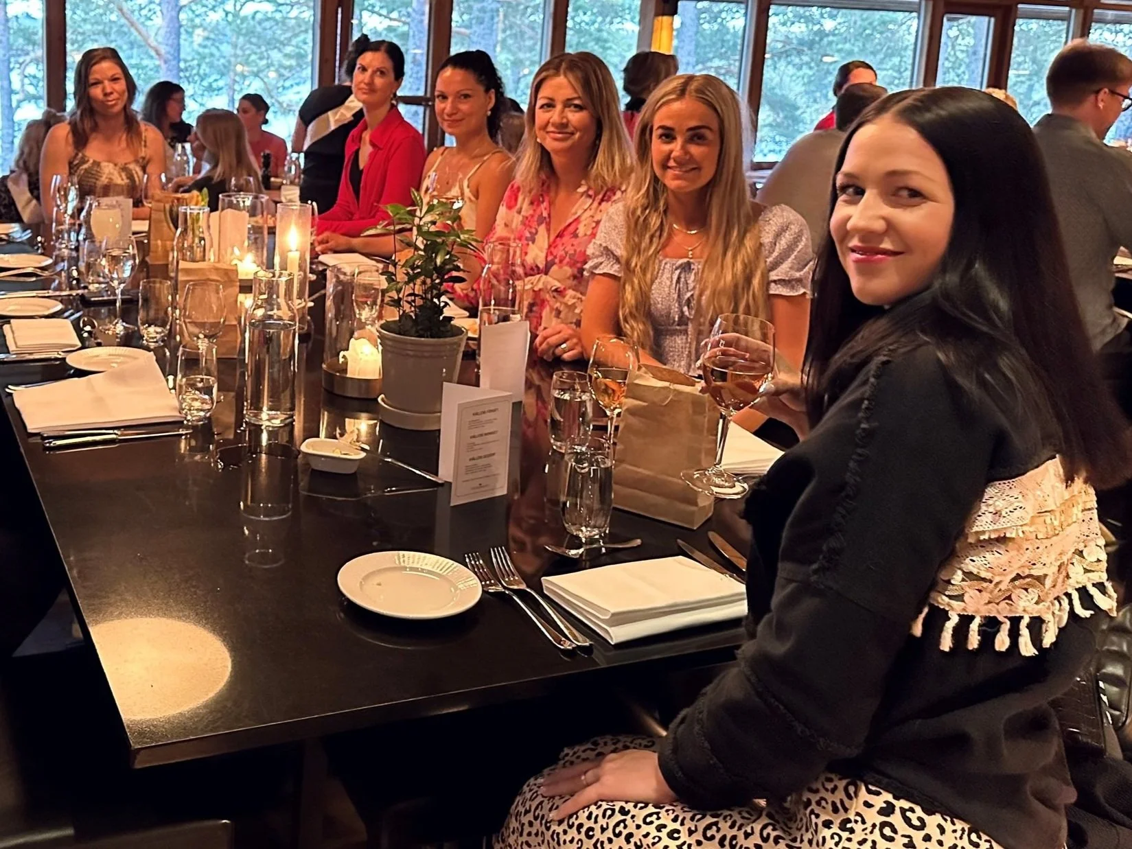 En grupp kvinnor sitter vid ett dukat restaurangbord under en middag, med levande ljus och dryck.
