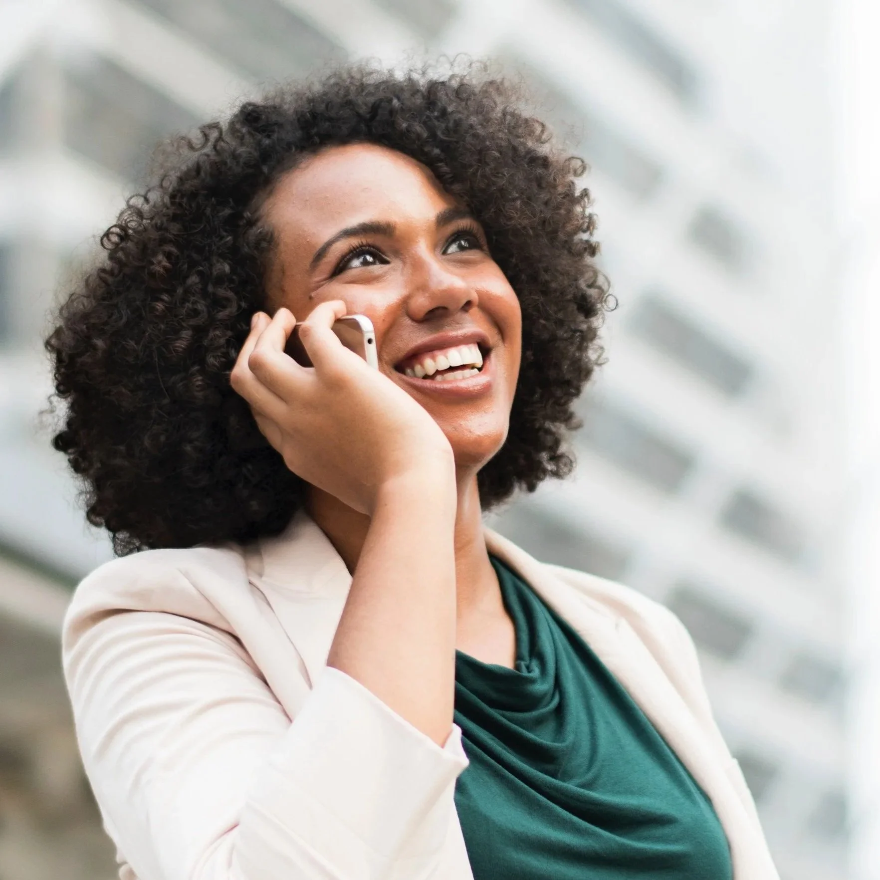 Smiling woman with curly hair talking on her cell phone inside a modern building.