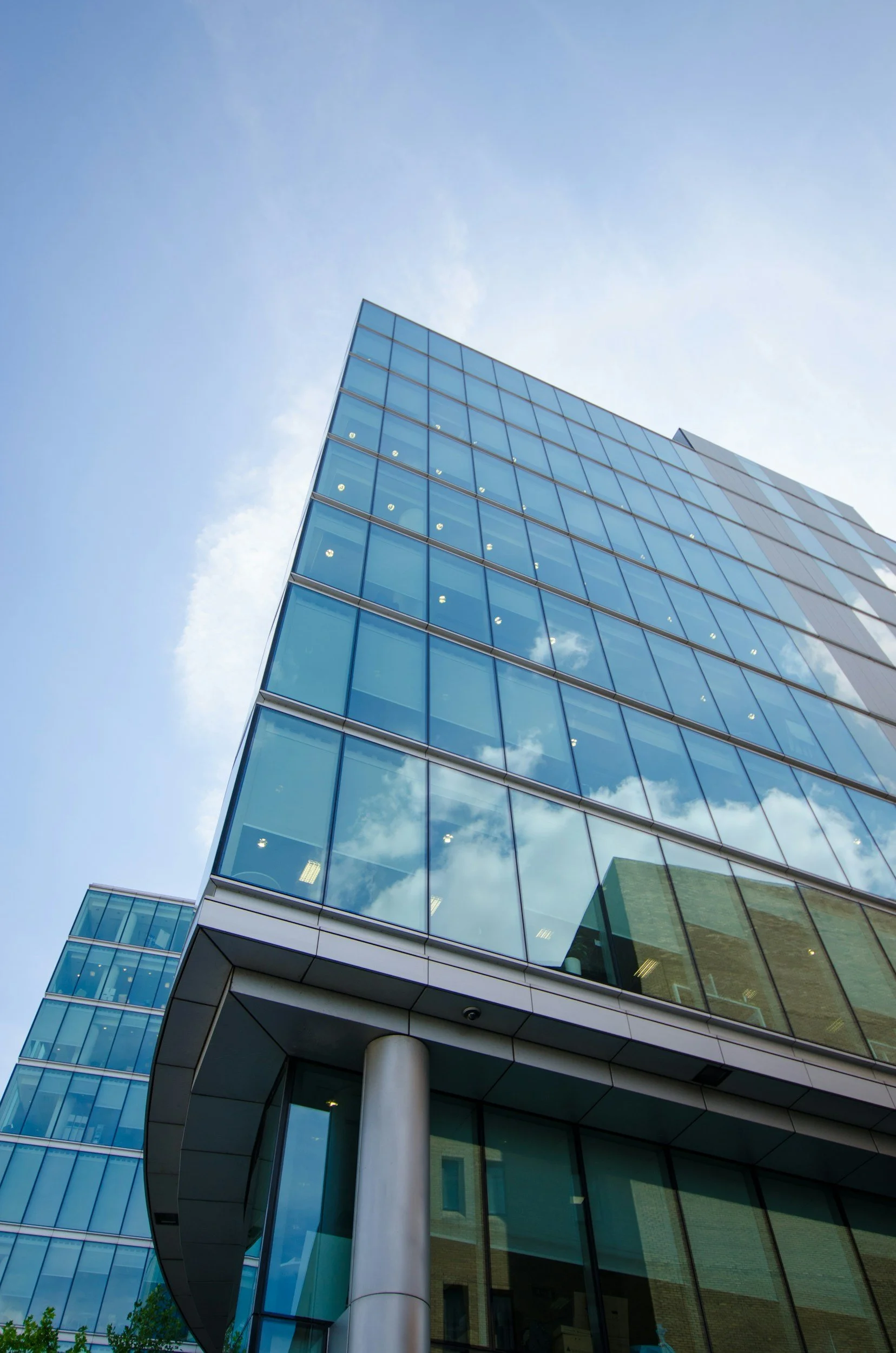 Modern glass office building with reflective windows against a blue sky with some clouds.