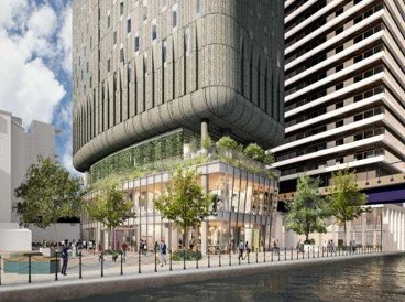 Street view of a modern building with glass storefronts, trees, and people walking, in an urban setting.