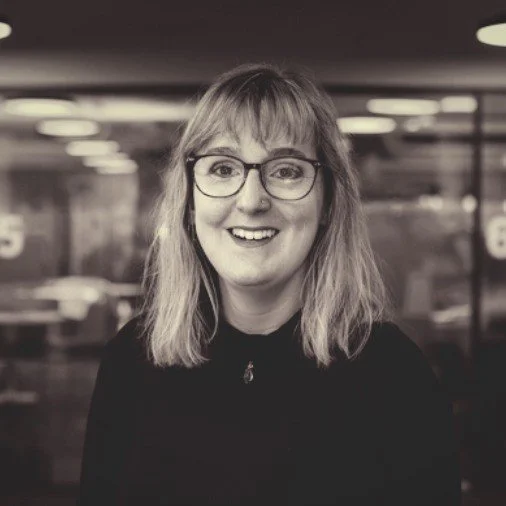 Portrait of a smiling woman with glasses and long hair in an office setting.
