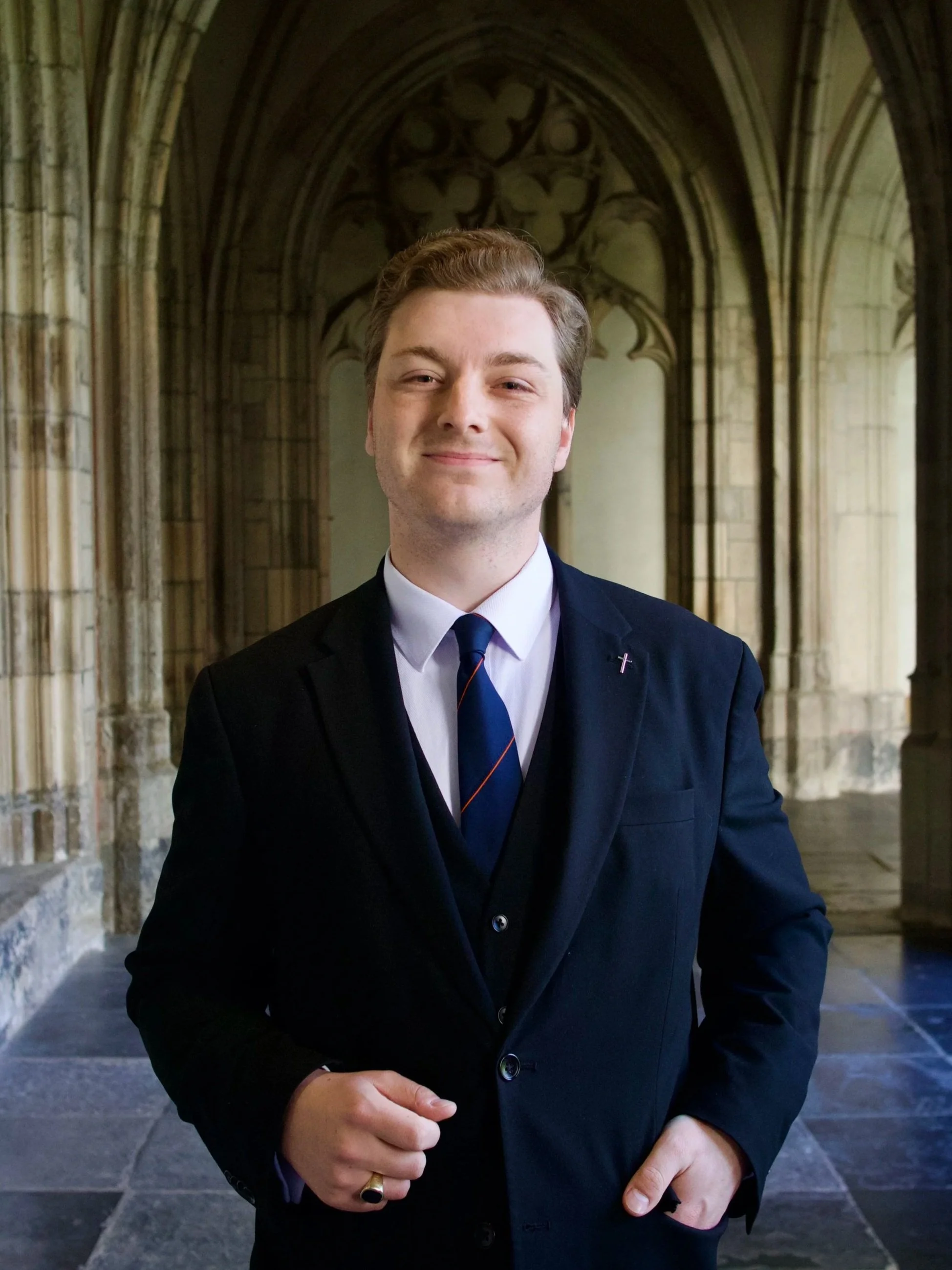 Man in een zwarte pakken met stropdas, staand binnen een historische kerk met gotische architectuur.