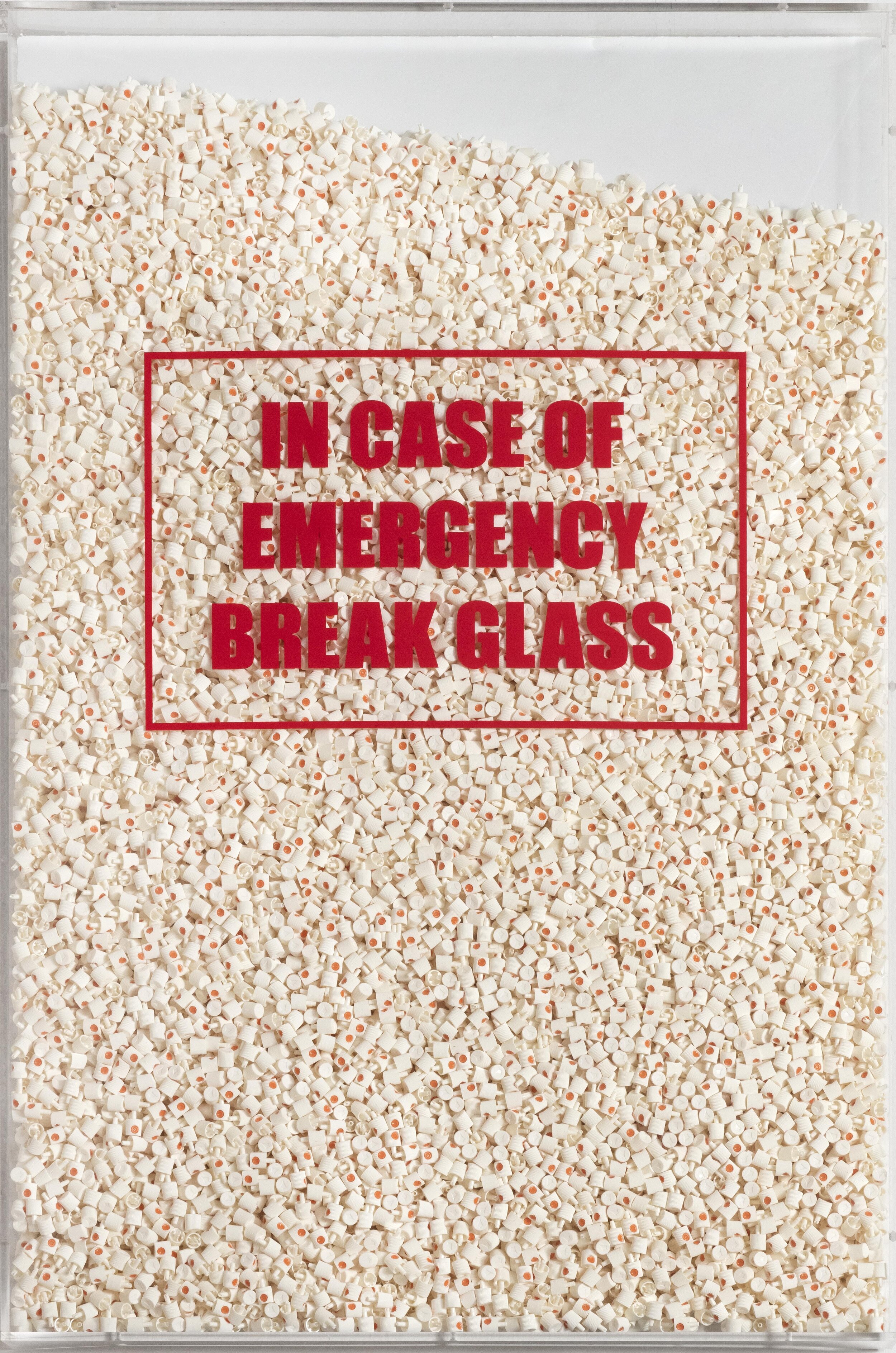 A large container filled with numerous small white plastic pieces and a sign that reads, "In case of emergency break glass" in red letters.