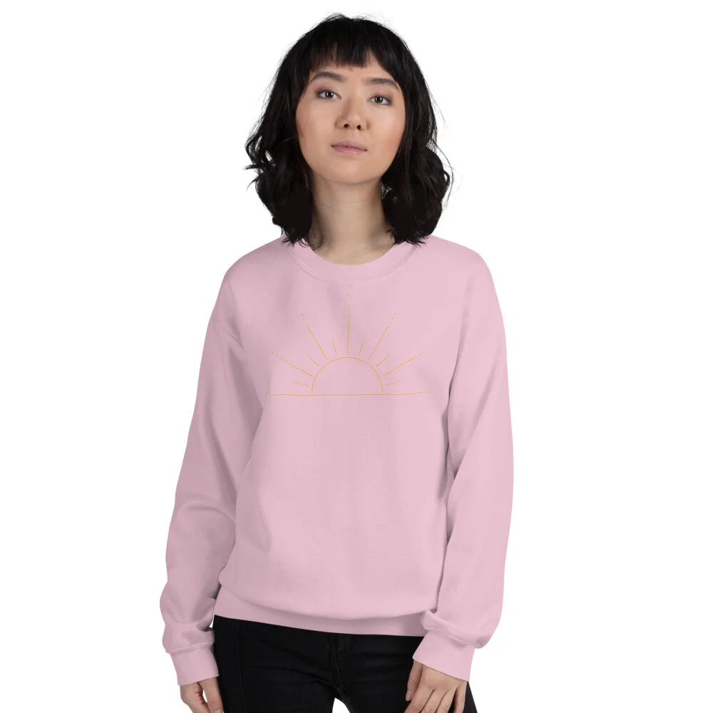 a woman in a pink sweatshirt with an sketch illustration of half a sun with rays of light