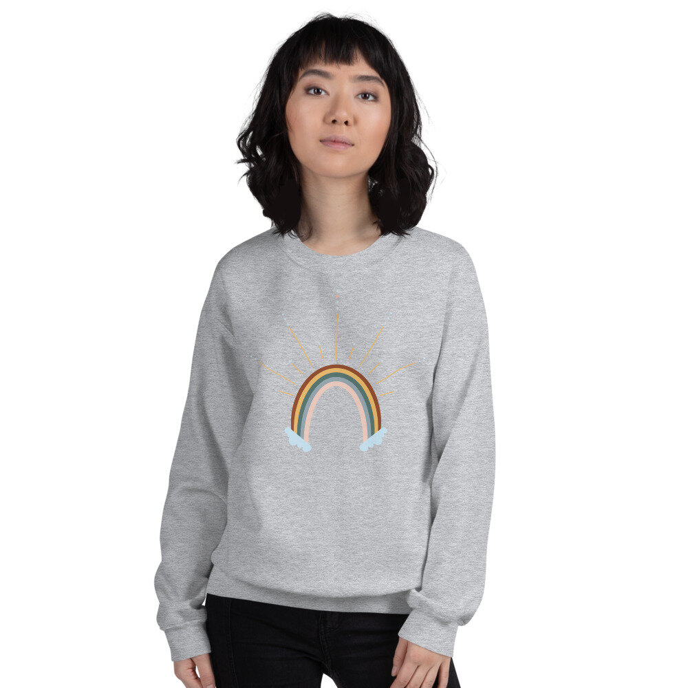 woman in a light grey sweatshirt with an illustration of a colorful rainbow and clouds