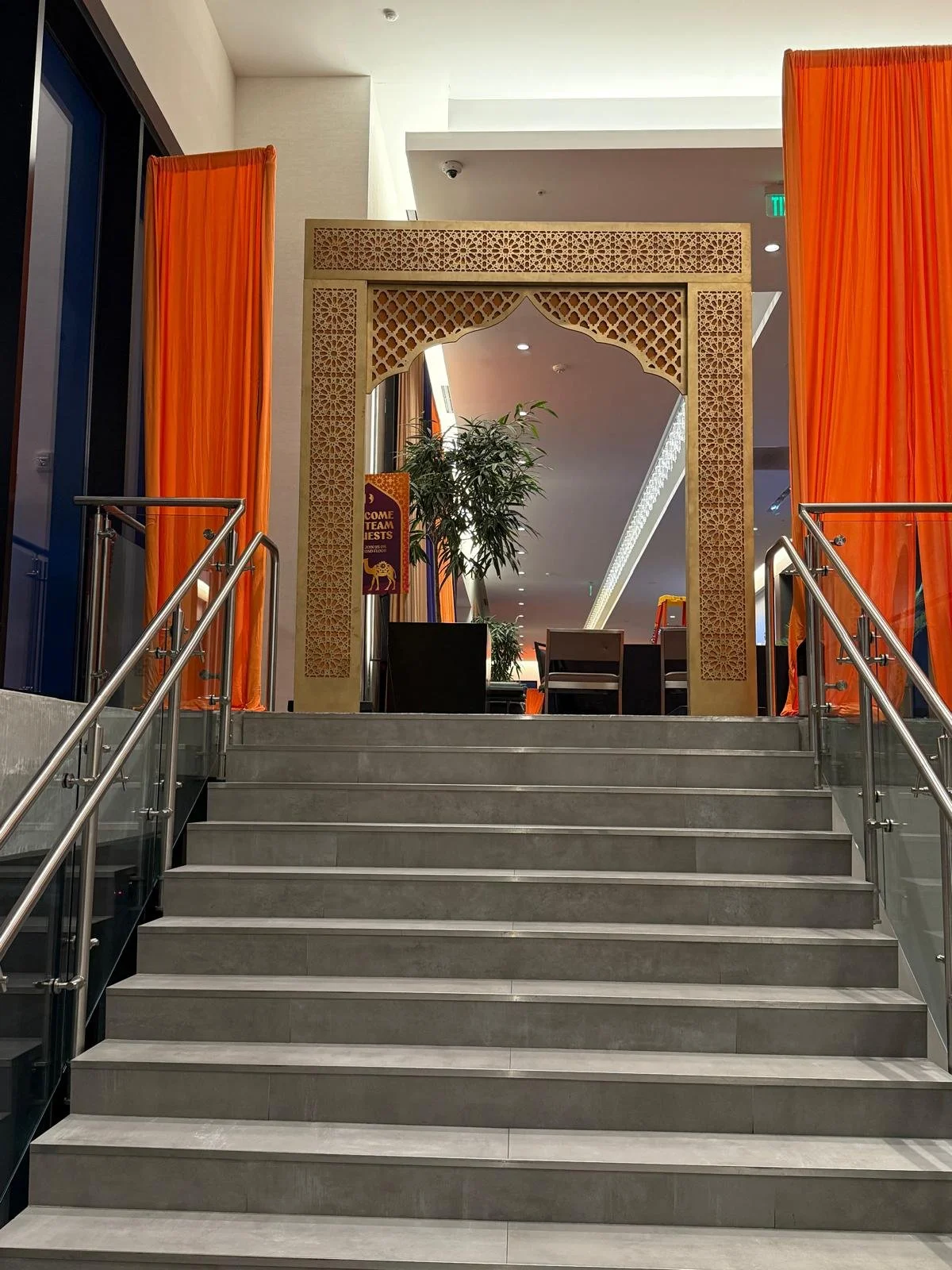 Indoor staircase leading up to a decorated lounge area with orange curtains, a decorative archway, plants, and seating visible in background.