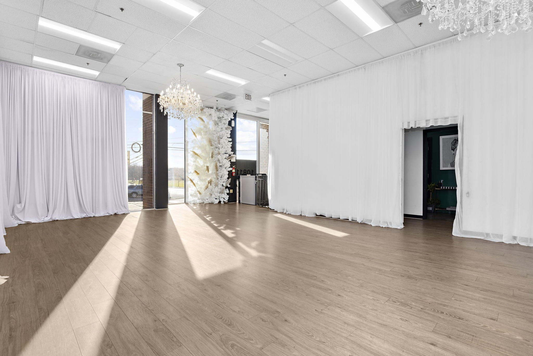 Spacious room with wooden floor, white curtains, and a chandelier.