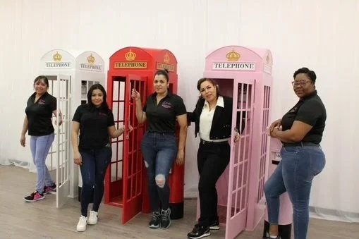 Five women standing beside vintage phone booths in different colors, smiling and posing for the photo.