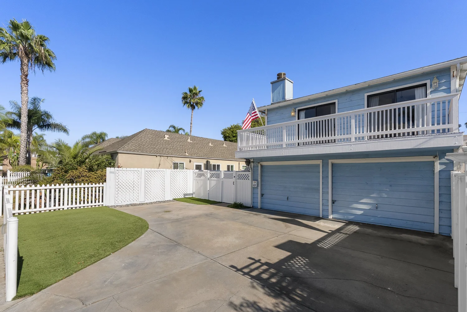 Front of the property with driveway, two garage doors, lawn and palm trees