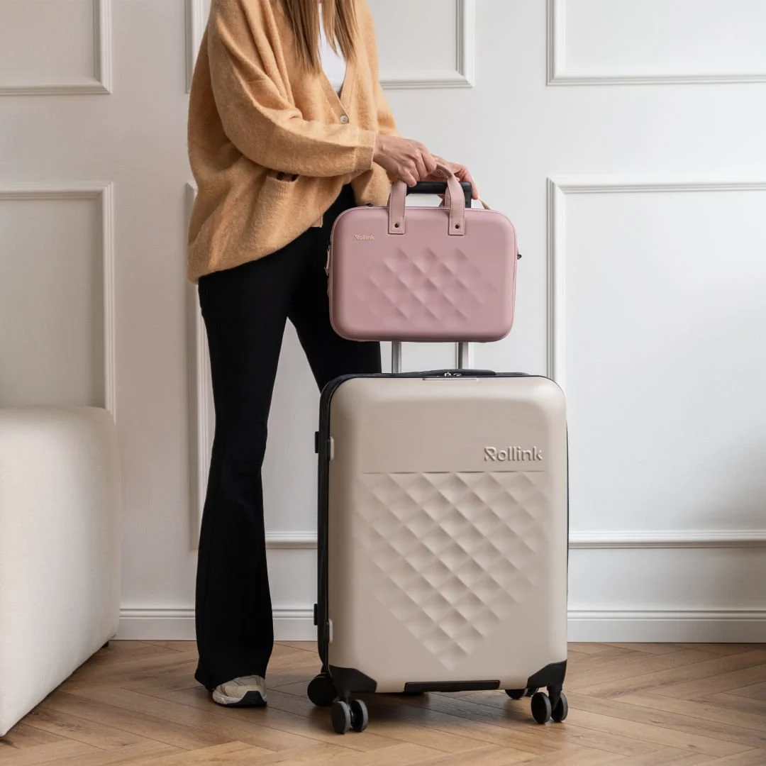 Traveler standing beside a beige hard shell suitcase with a small pink travel case on top