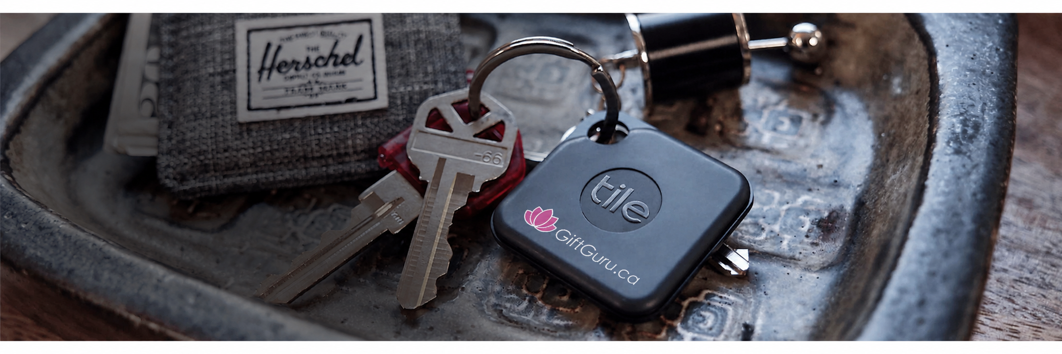 Tile key tracker with GiftGuru logo and Herschel wallet in decorative tray