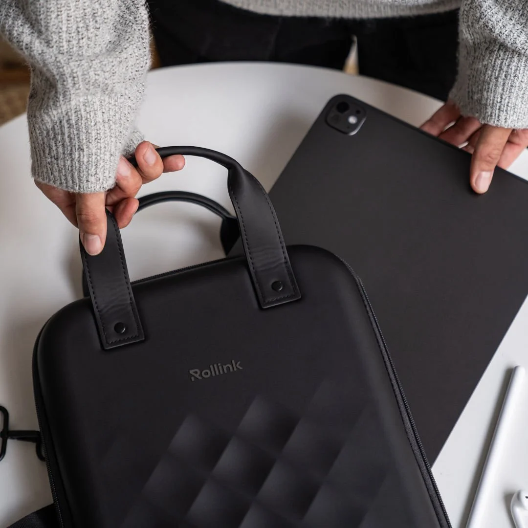 Hands sliding a laptop into a black Rollink Go vertical hard shell case on a table