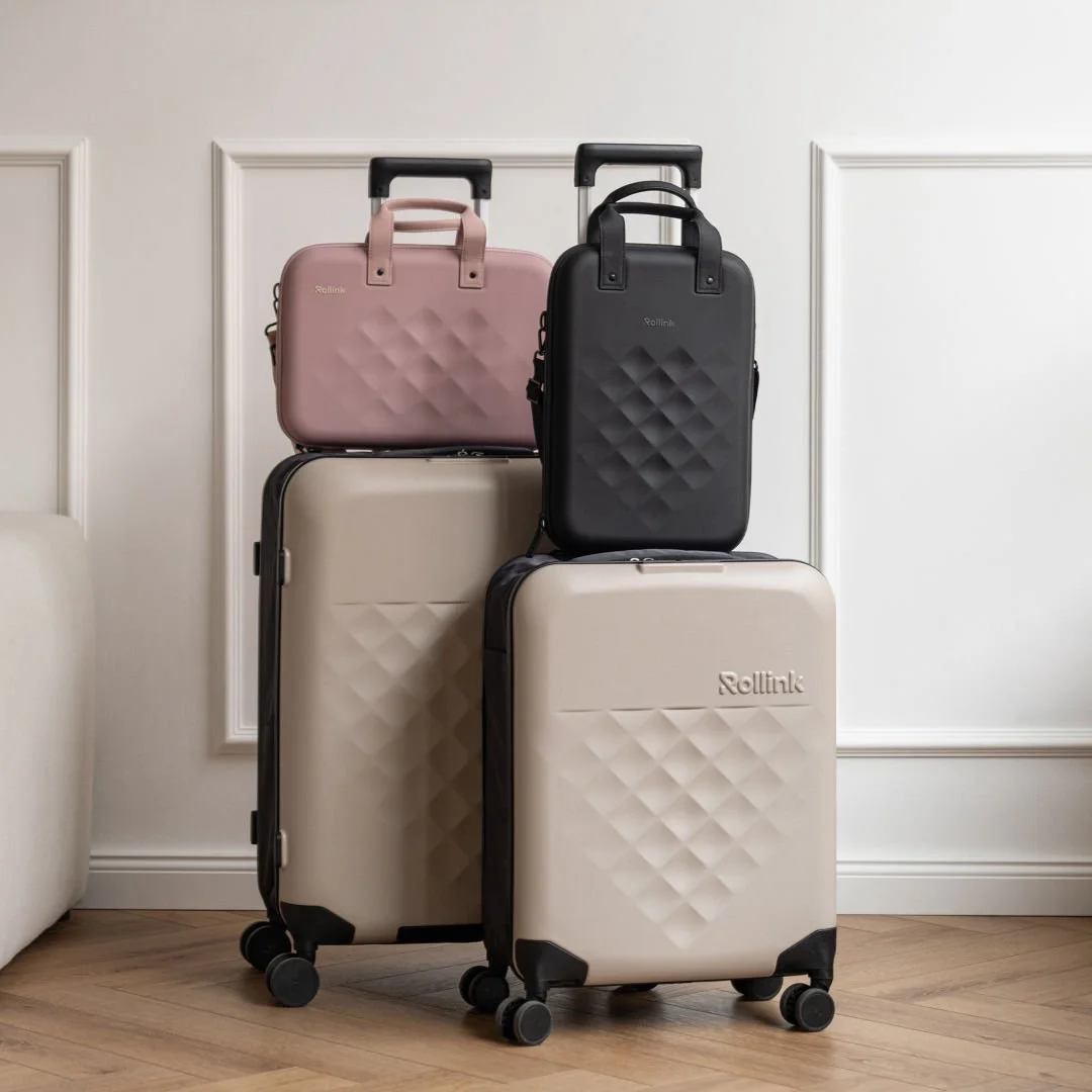 Beige hard shell suitcases stacked with pink and black Rollink laptop cases on top