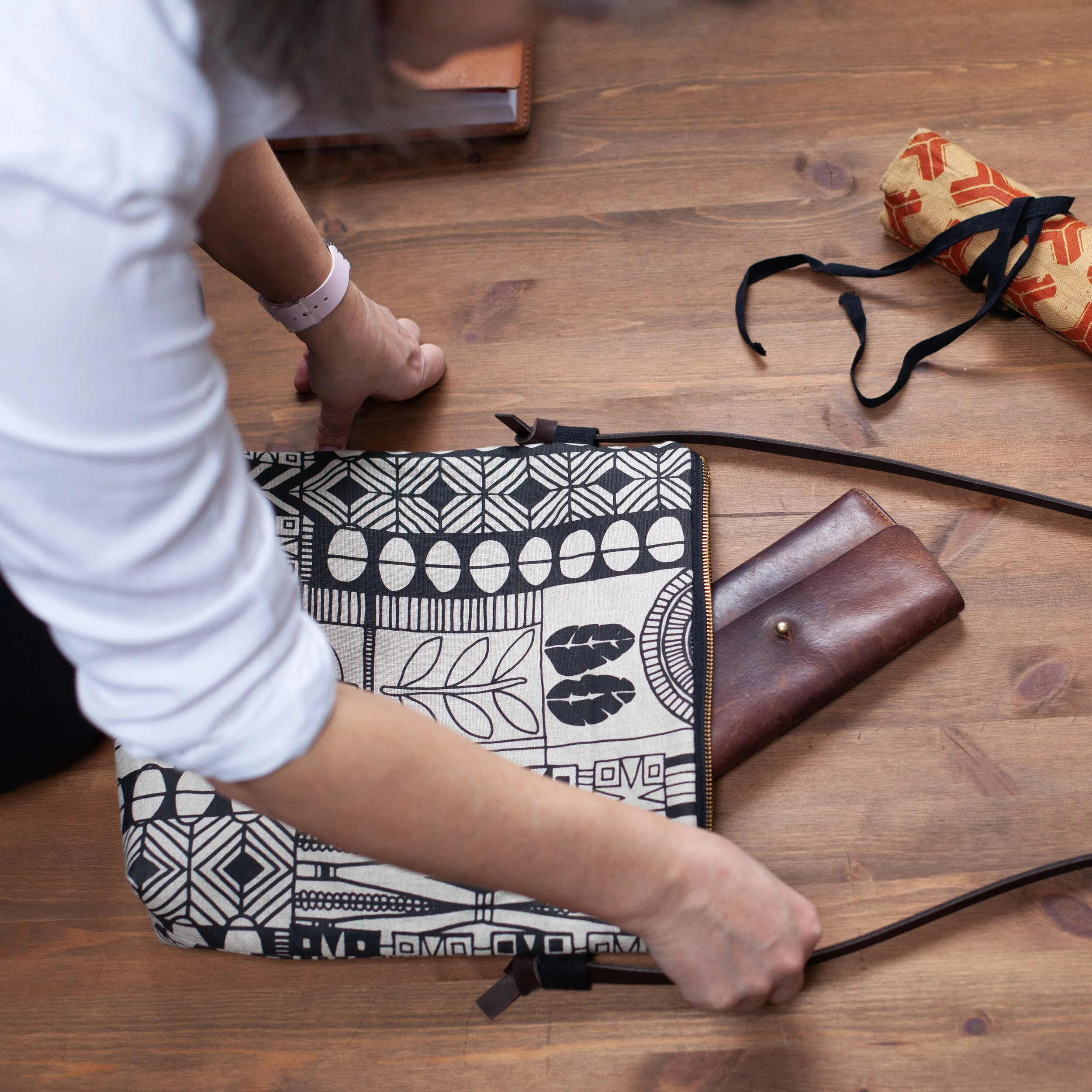 Hands arranging a handmade product and props on a wooden table for a product photograph.