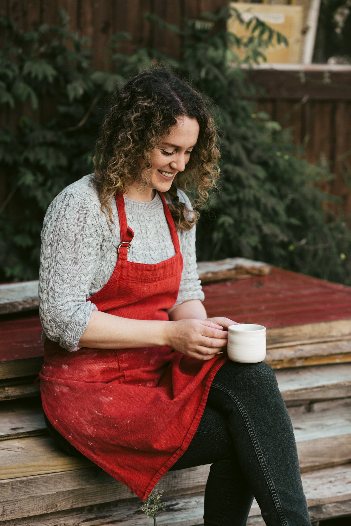 Ceramic maker Chloe Dowds holding one of her handmade cups while seated outdoors.