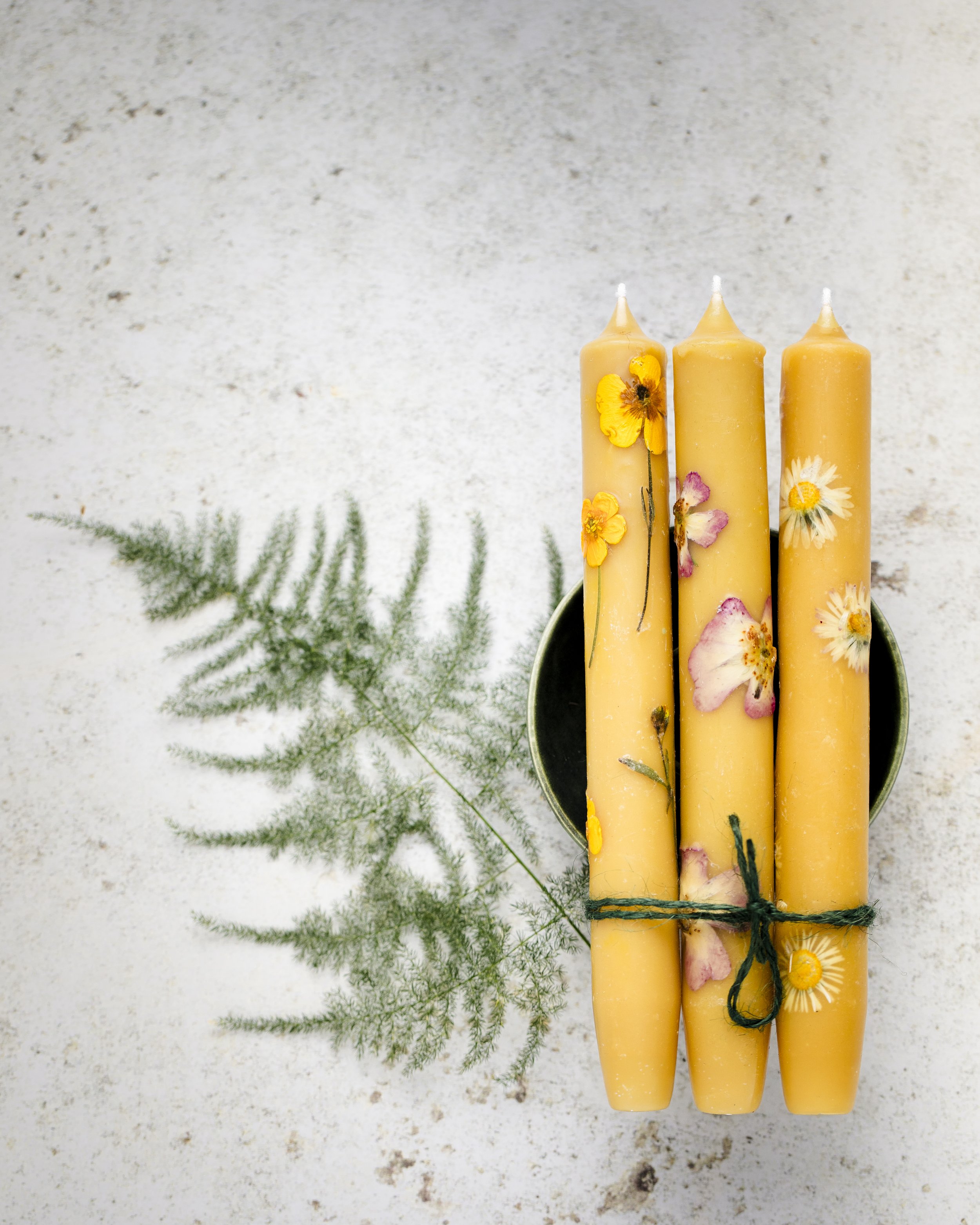 Three yellow artisan candles photographed together against a pale background with greenery.