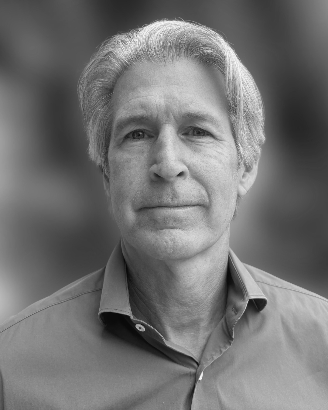 Black and white portrait of a middle-aged man with gray hair, wearing a collared shirt, looking directly at the camera.