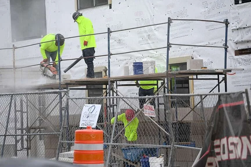 Construction workers wearing high-visibility clothing working on a building site, with some using tools and others handling materials on scaffolding.