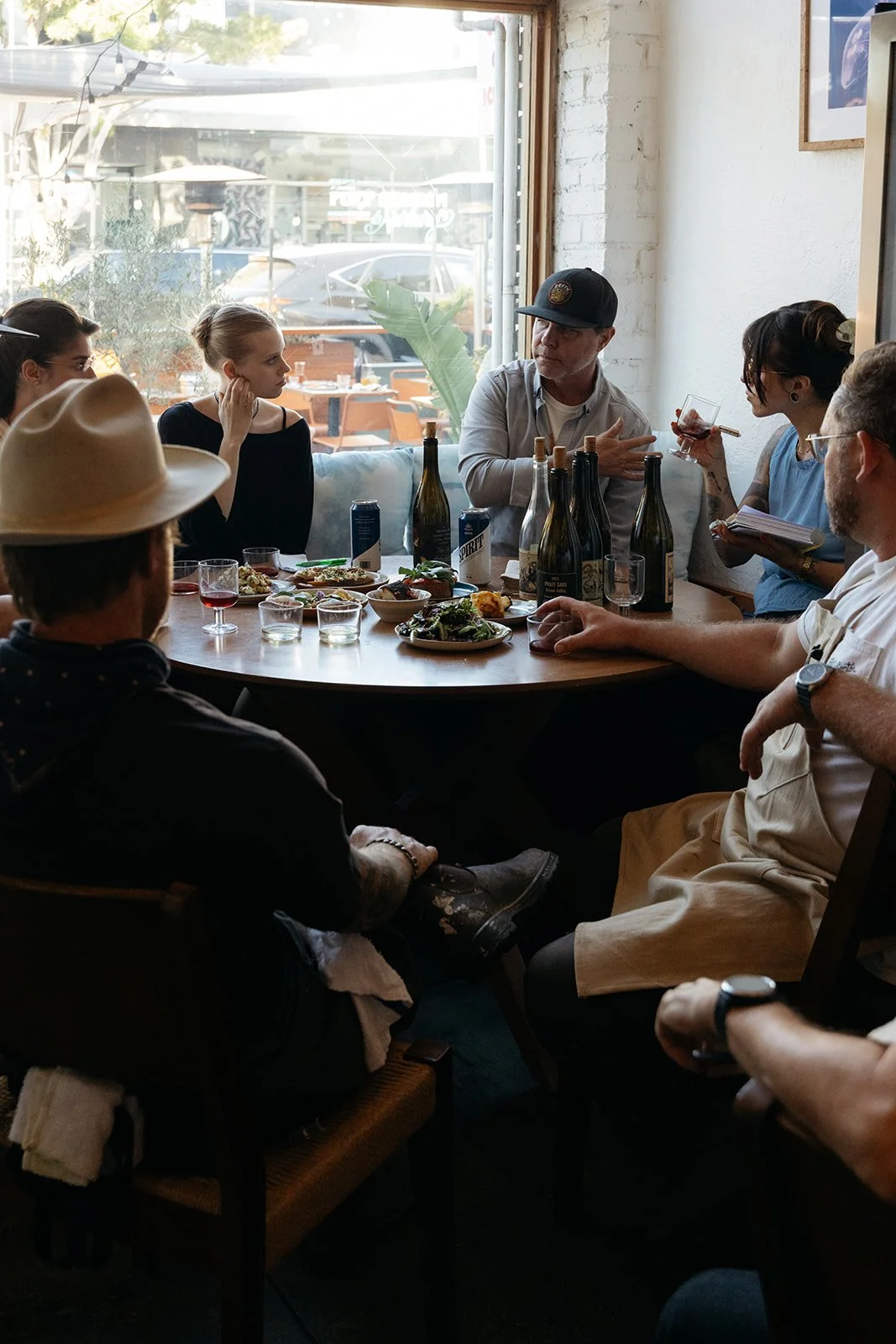 People sitting around a table filled with wine bottles and dishes inside Crudo e Nudo