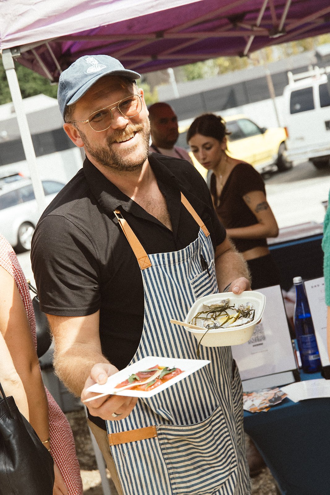 Chef & Owner Brian Bornemann holding plates of crudo & oysters by a tent during an outdoor event