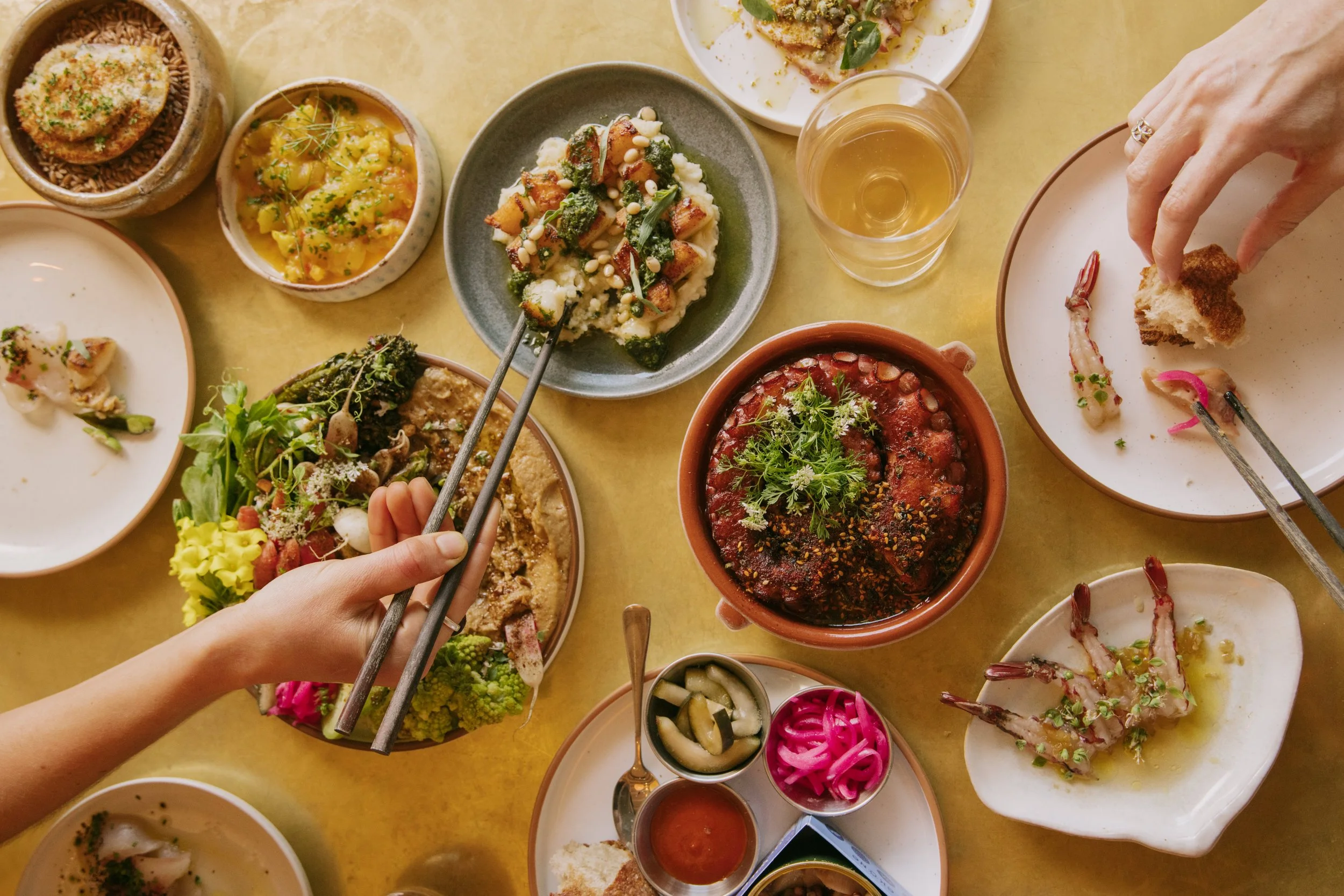 Variety of Crudo, Cooked Seafood, Mezze Plate and Glasses of Wine with Hands Holding Chopsticks