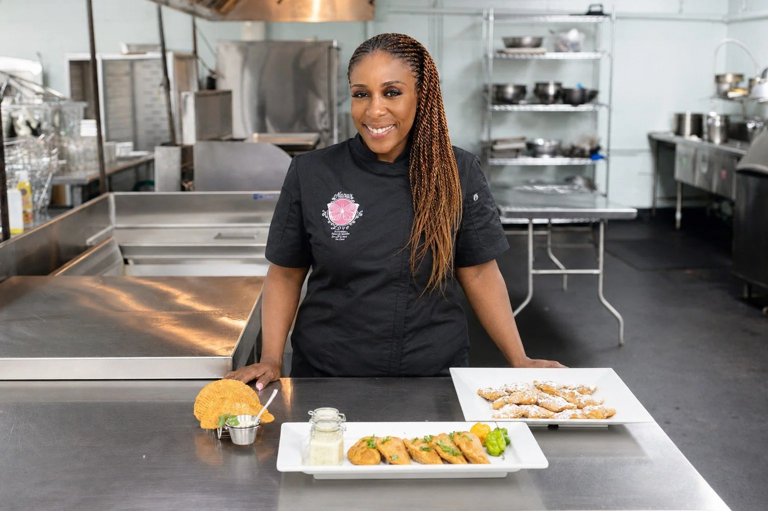 Nana’s Love chef presenting freshly prepared empanadas and catering dishes in a commercial kitchen.