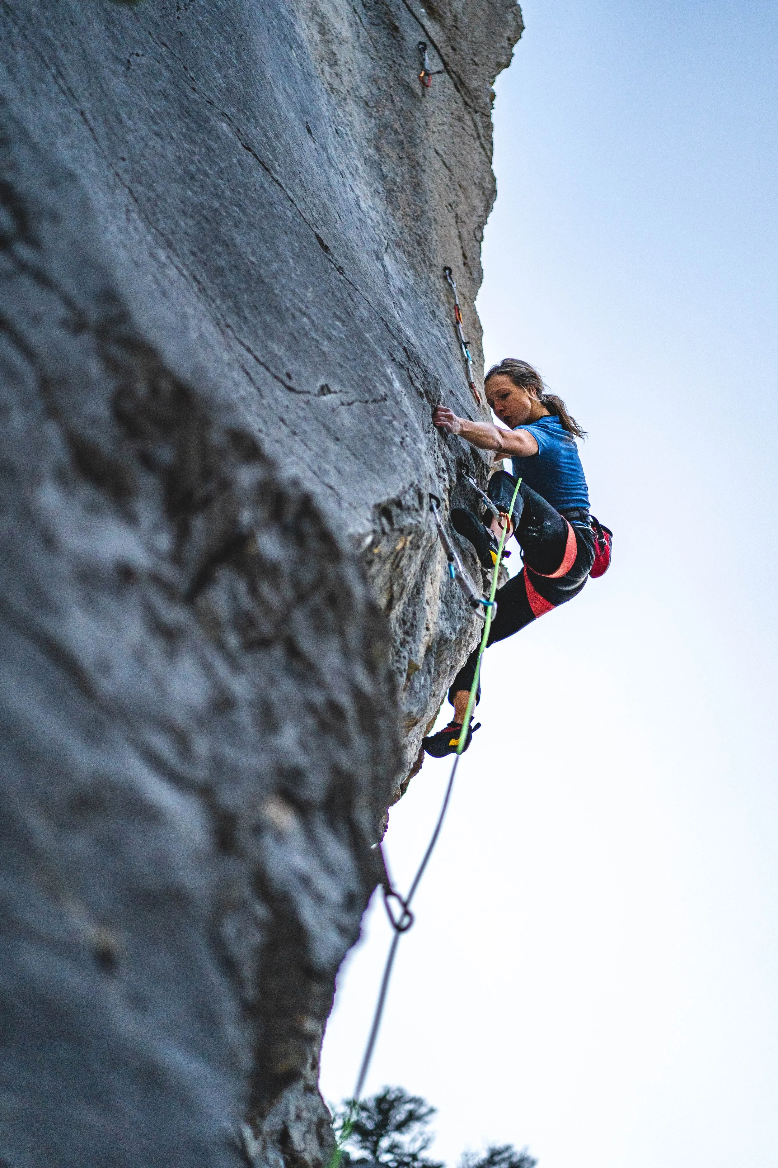 A young man rock climbing on a steep, outdoor rock face, smiling at the camera.