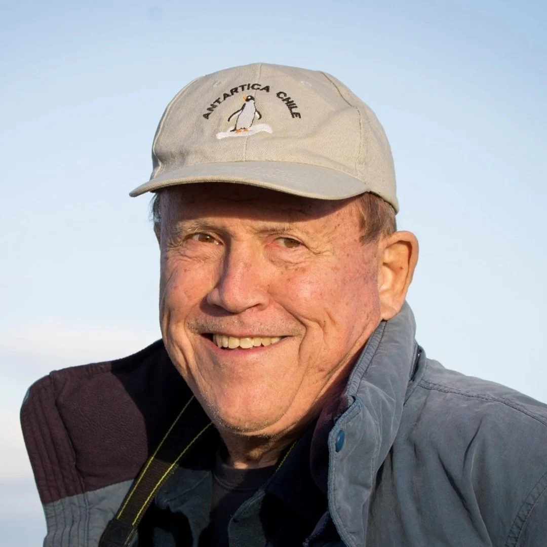 A smiling man wearing a beige cap with "Antarctica Chile" and a penguin logo.