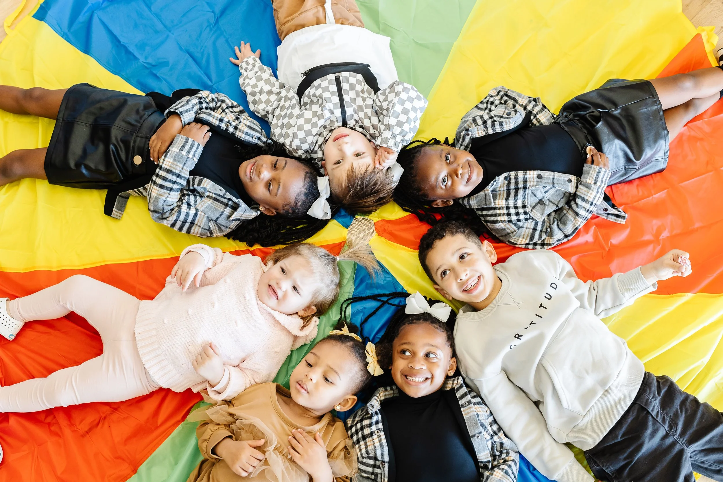 Children lying on a colorful parachute, smiling and playing together in a group.
