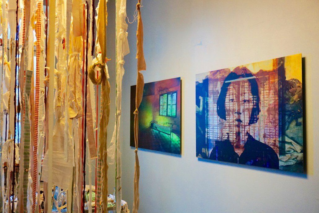 Installation with fabrics to the left and Photo from S-21, Cambodia on the wall