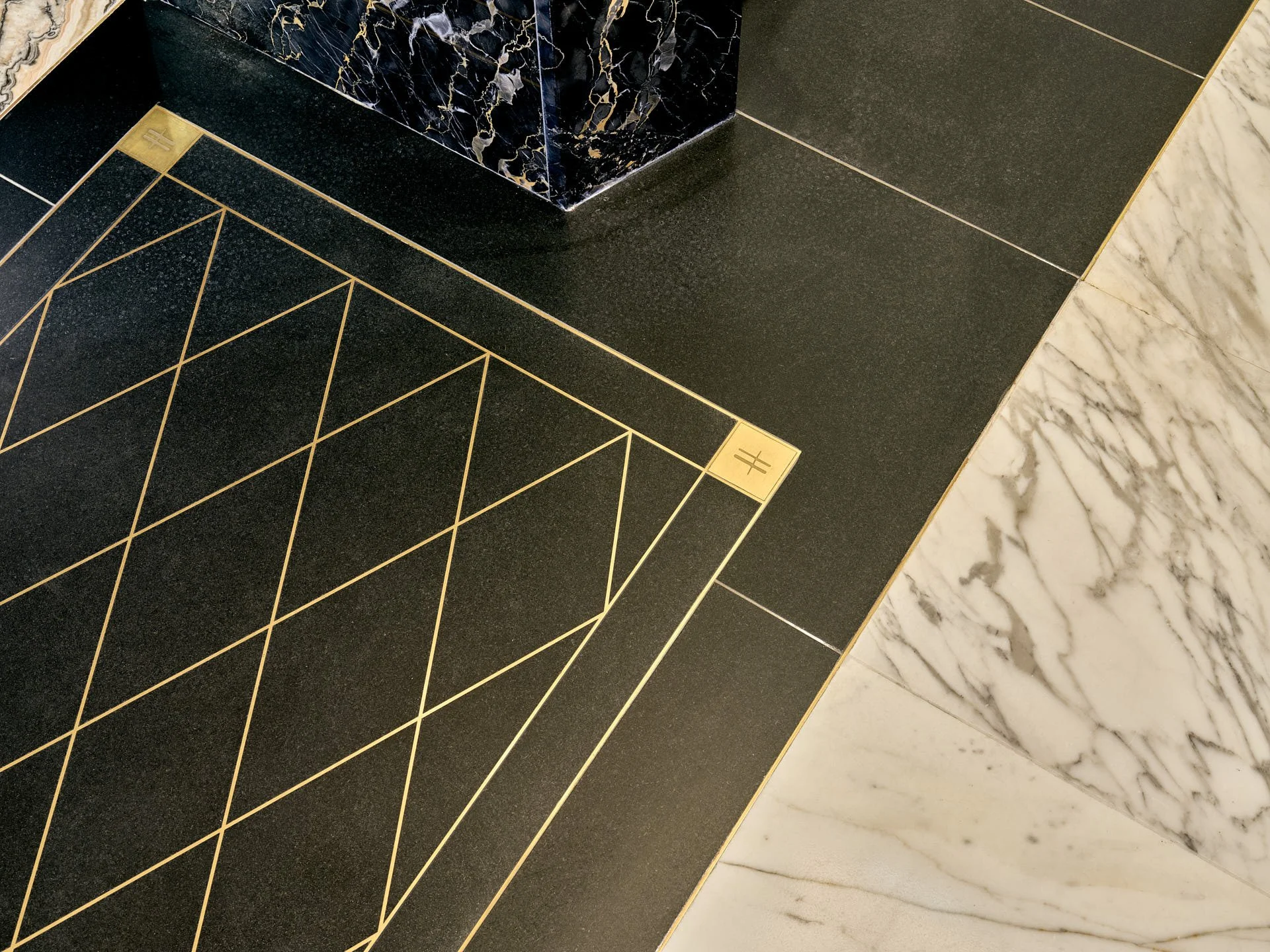 Close view of Zimbabwe Black granite crossed by fine brass lines beside pale Calacatta Oro flooring and a dark marble display base. Fabrication and installation by stoneCIRCLE - photo Marco Joe Fazio Studio.