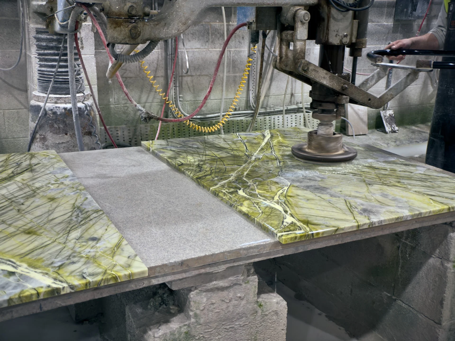 A mason operates the Jenny Lind radial-arm polisher over green stone pieces on a workshop bench.