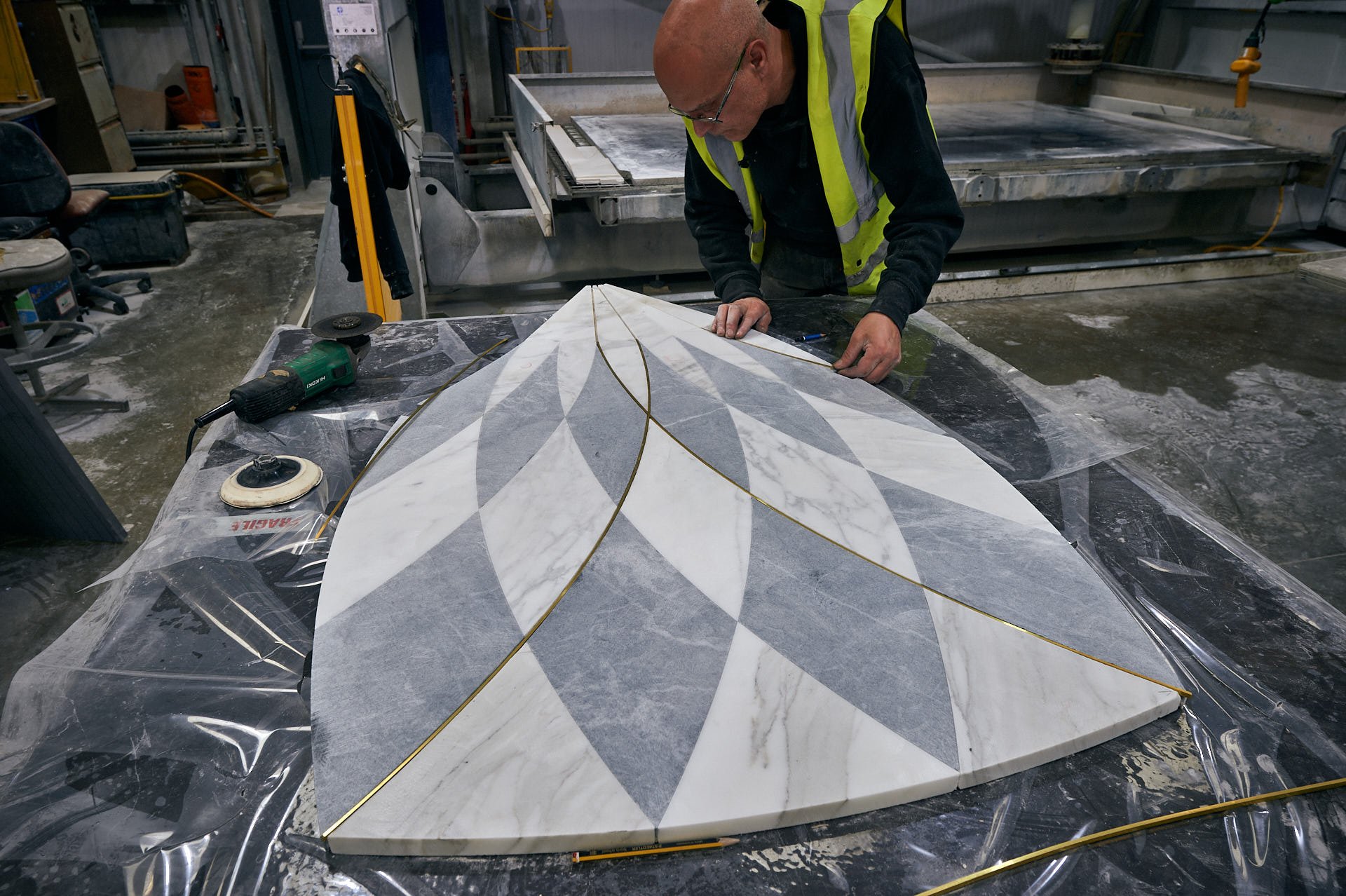 Craftsperson leaning over a curved Calacatta Oro and Blue Masaccio floor section while checking its radiating brass inlay lines. Fabrication by stoneCIRCLE - photo Marco Joe Fazio Studio.