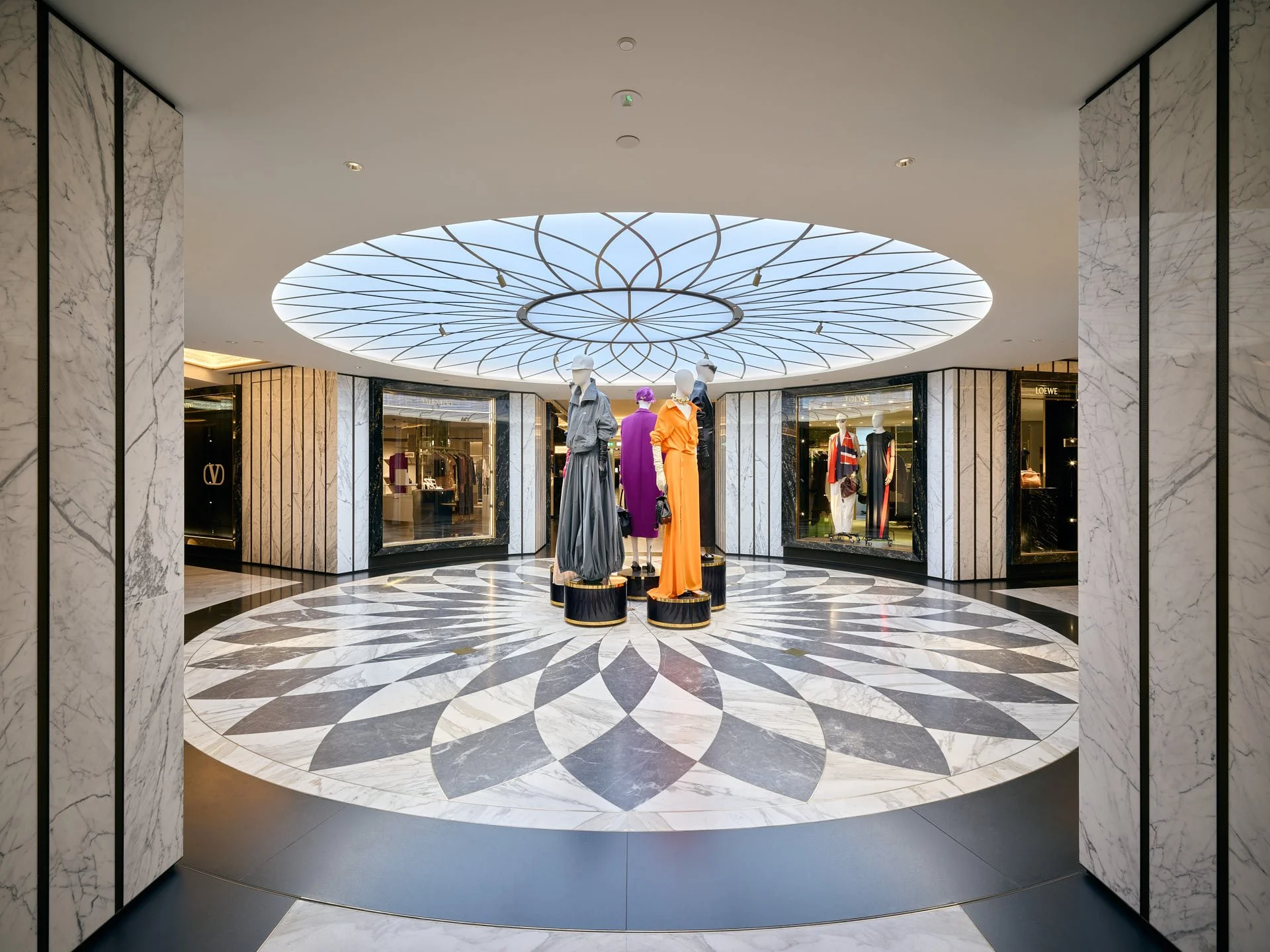 Symmetrical view into Harrods Women's Superbrands with a circular white and blue-grey stone floor, dark border and mannequins at its centre. Fabrication and installation by stoneCIRCLE - photo Marco Joe Fazio Studio.