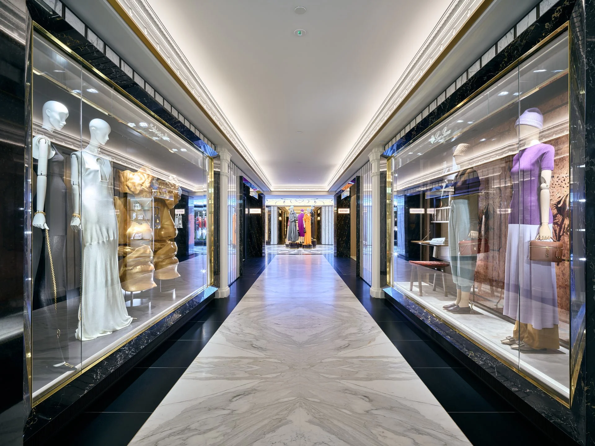 Long Harrods corridor with veined pale stone flooring, dark borders, marble wall panels and illuminated fashion displays on both sides. Fabrication and installation by stoneCIRCLE - photo Marco Joe Fazio Studio.
