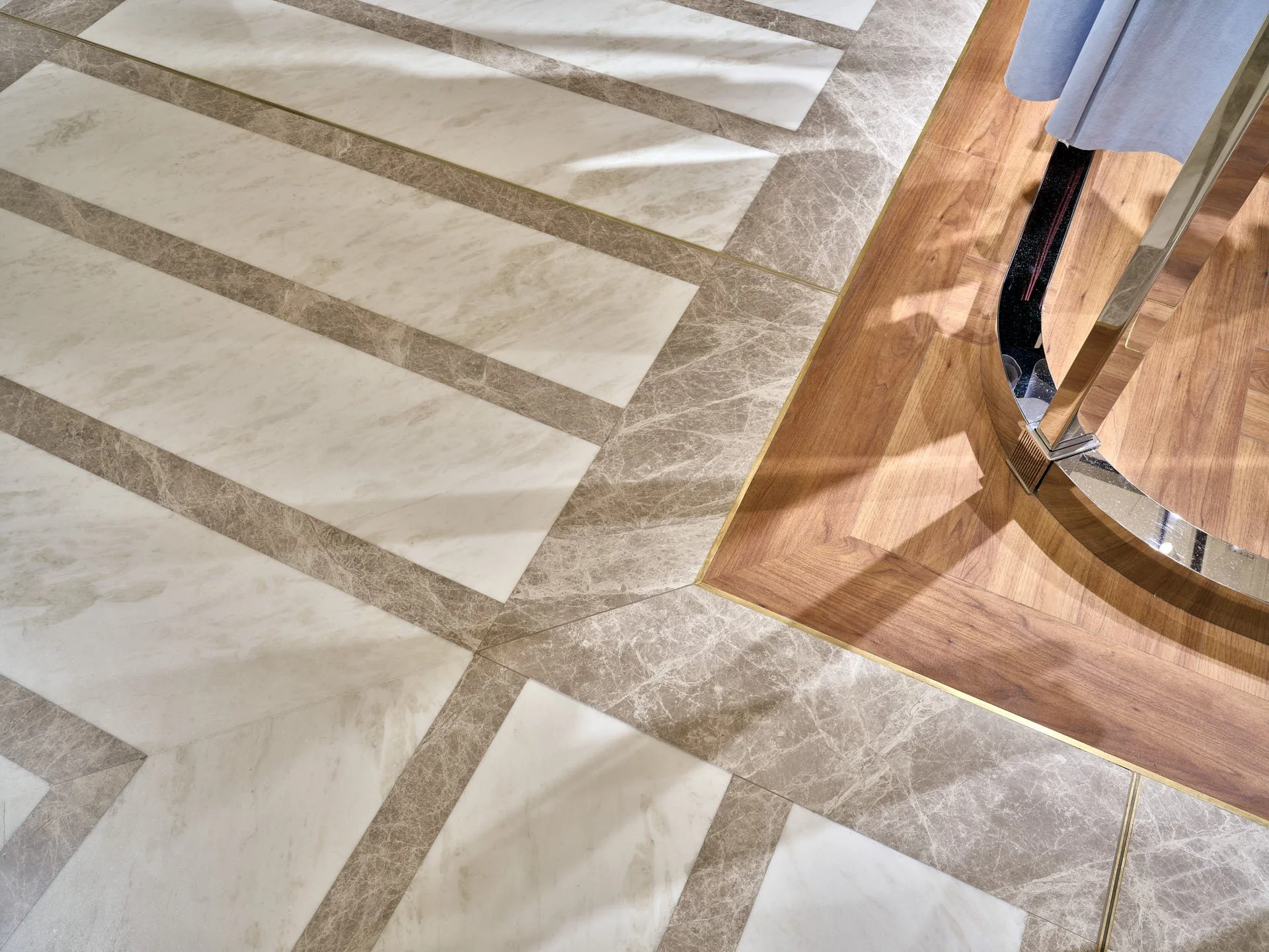 Close view of white and grey marble floor bands meeting timber flooring and a curved metal retail display by stoneCIRCLE - photo Marco Joe Fazio STUDIO