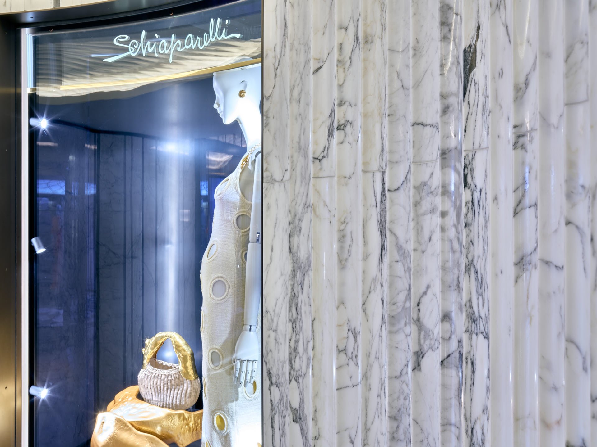 Close-up of polished fluted Calacatta Oro wall panels beside an illuminated fashion display containing a mannequin and gold accessories. Fabrication and installation by stoneCIRCLE - photo Marco Joe Fazio Studio.